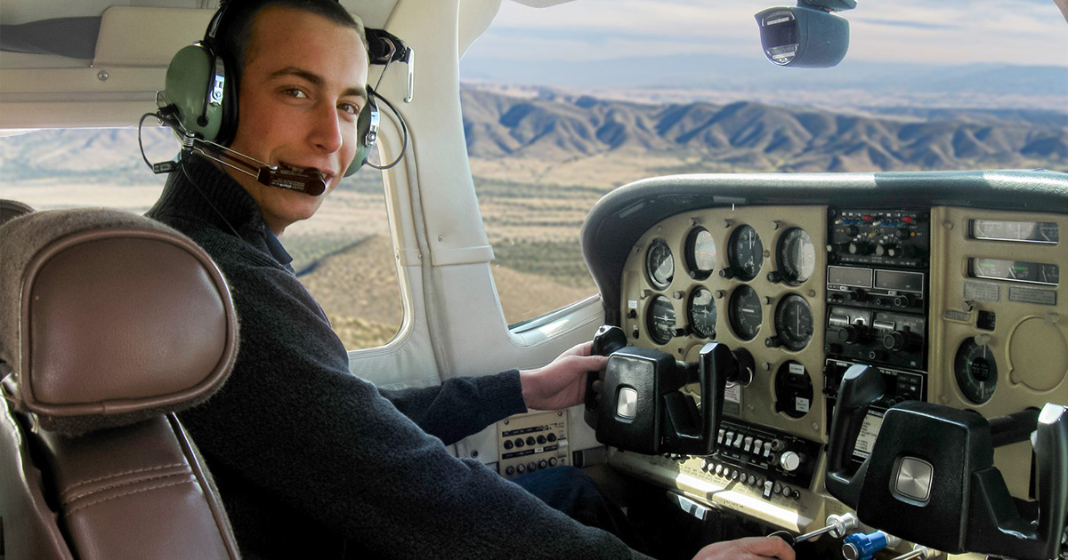 A pilot in the cockpit of a private plane over a western landscape.